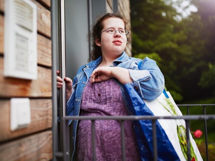 Eine junge Frau steht vor einer Wohnungstür. Sie hat eine sogenannte geistige Beeinträchtigung.